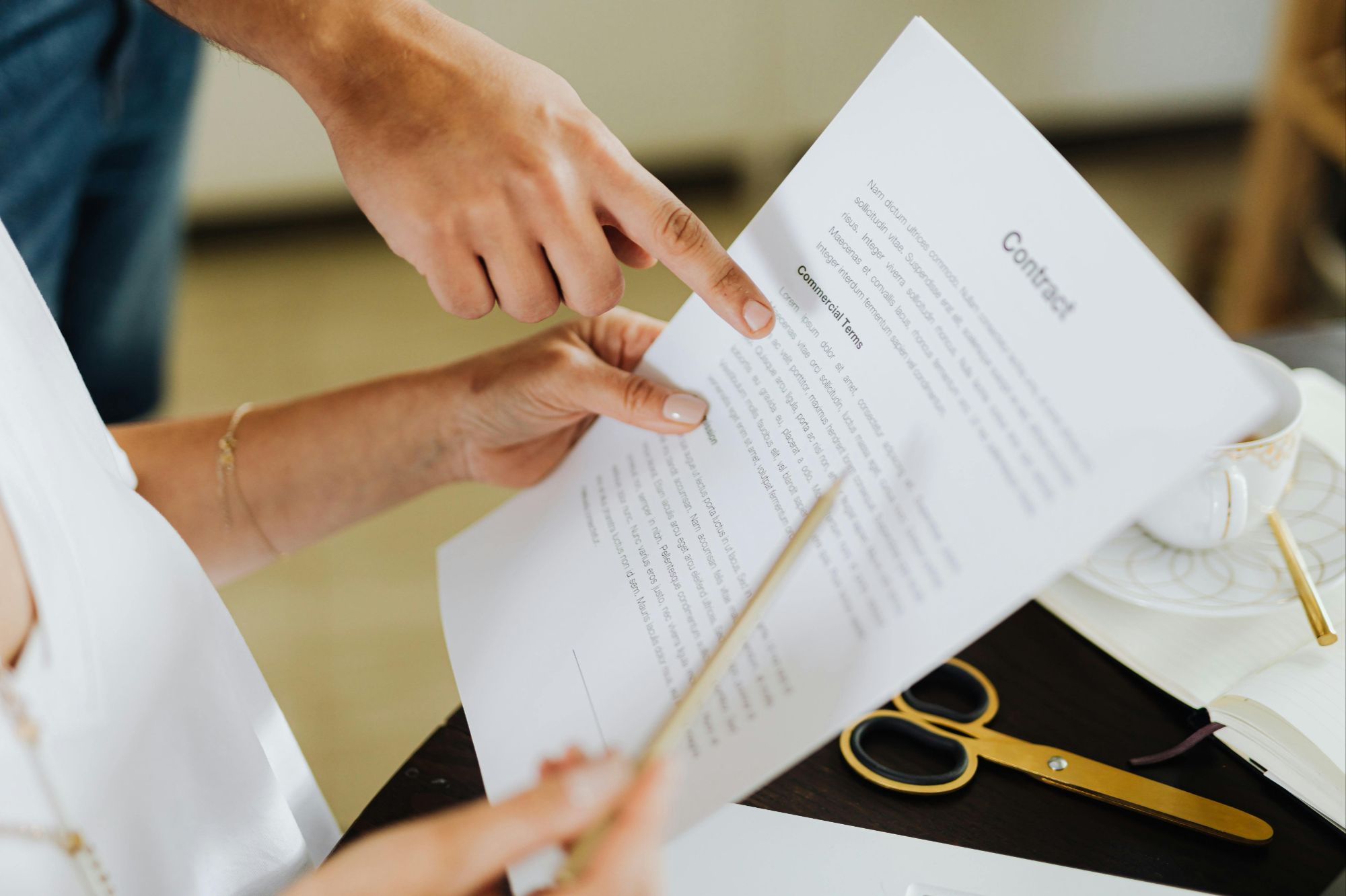 Two people reviewing real estate contract with Commercial Terms at Boulder, CO office desk with notebook, scissors, pen, and coffee cup.