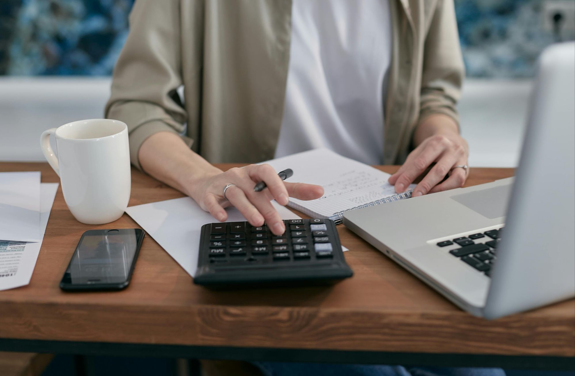 Person working at desk with calculator, laptop, papers, and coffee mug, symbolizing Boulder, CO real estate budgeting and home financing.