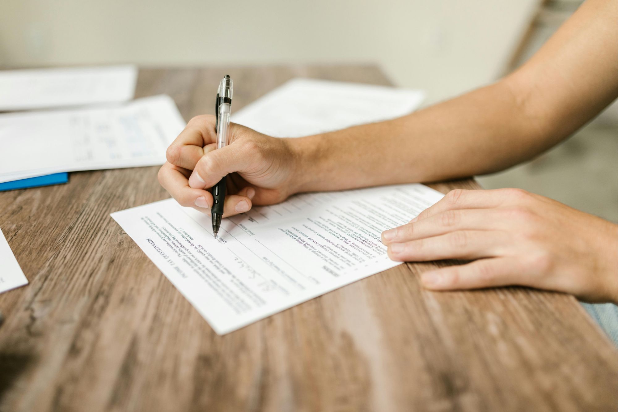 Close-up of hands filling out real estate paperwork on wooden table, representing Boulder, CO home buying and property transaction process.