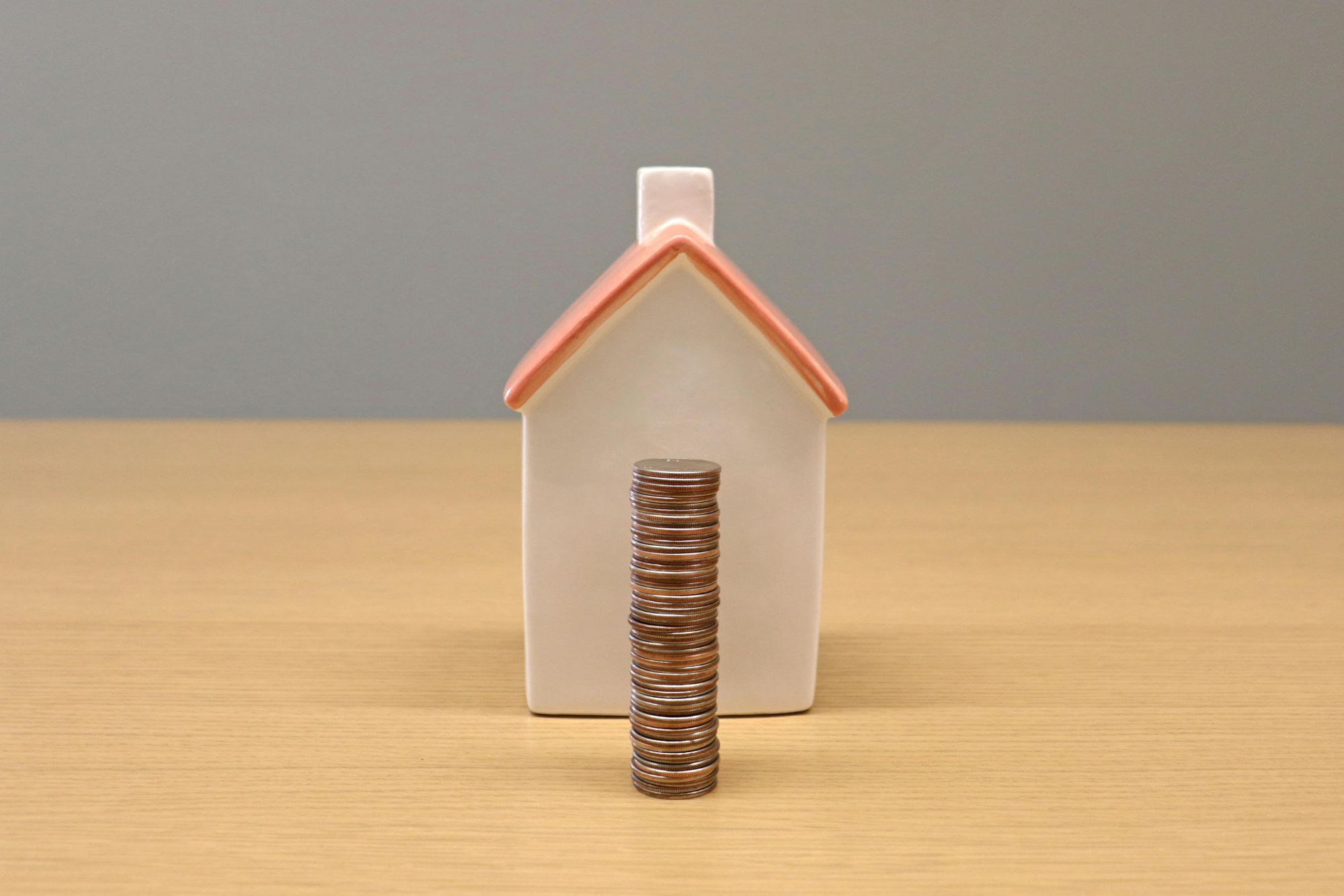 Stacked coins in front of a small house model representing home equity, property value, and real estate investment in Boulder