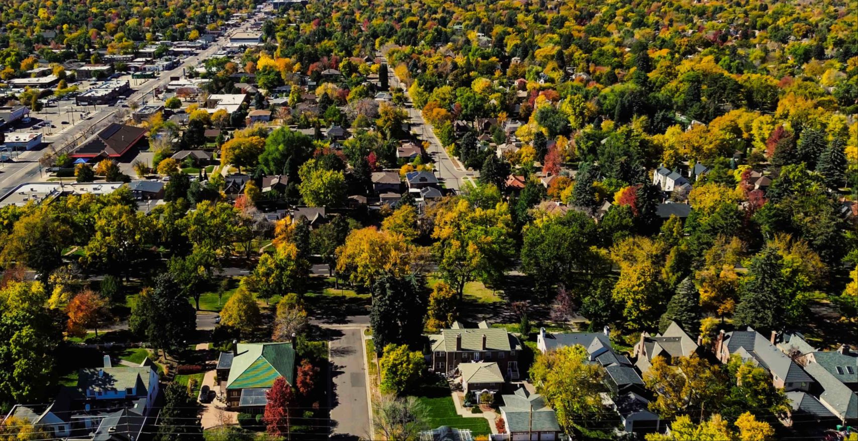 An aerial or drone shot showing a Boulder neighborhood grid with bike lanes, tree cover, and a commercial corridor visible.