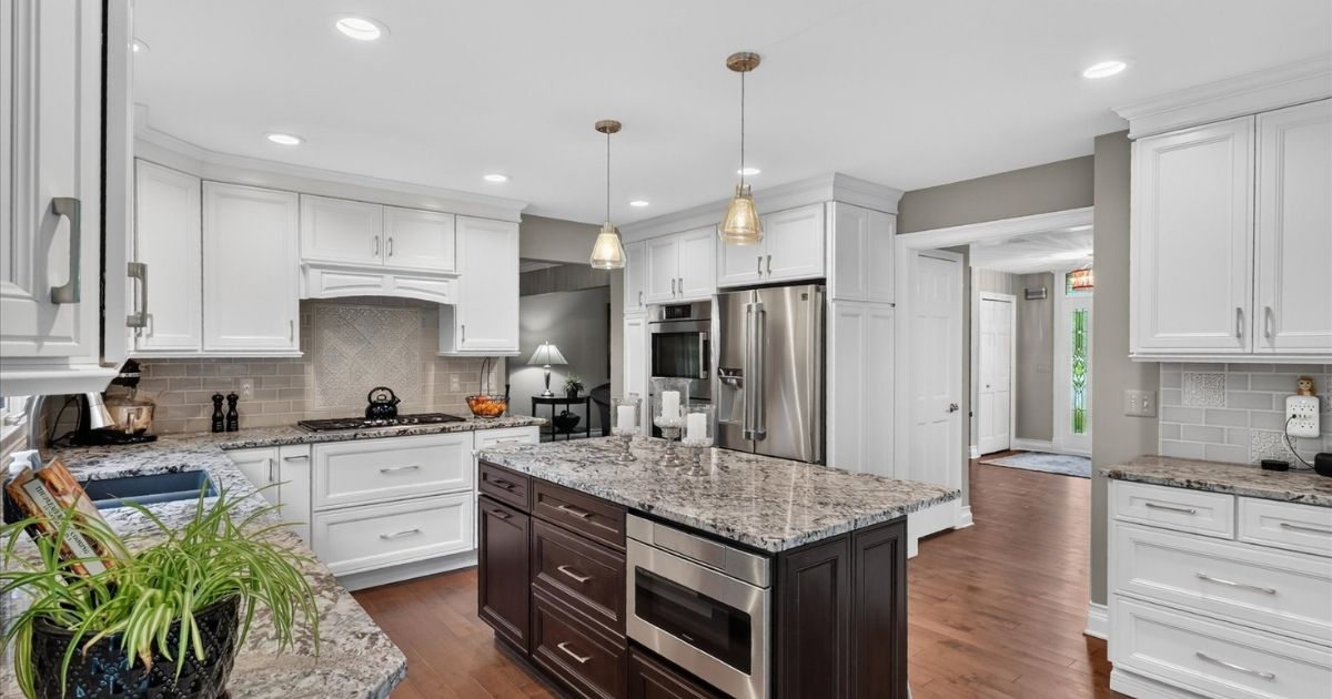 Remodeled kitchen with white cabinetry, contrasting island, stone countertops, stainless steel appliances, and pendant lights.