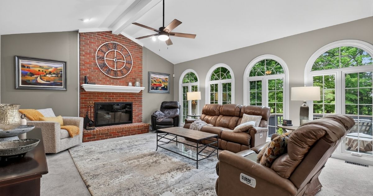 Family room with vaulted ceiling, brick fireplace, and large arched windows overlooking the backyard.