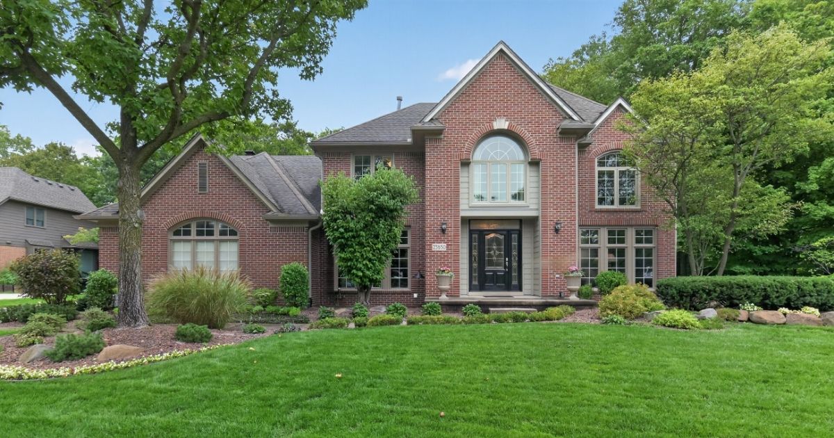 Two-story brick colonial with arched windows, mature trees, and landscaped front lawn in Novi's Walden Woods community.