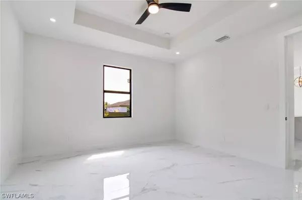 Bright bedroom with tray ceiling, modern ceiling fan, and large-format marble-look tile flooring in Cape Coral new construction home.