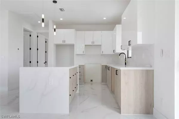 Modern Cape Coral new construction kitchen with quartz countertops, waterfall island, two-tone cabinetry, and sleek pendant lighting