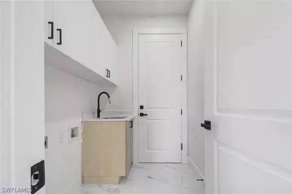 Modern laundry room with washer and dryer hookups, utility sink, and upper storage cabinets in Cape Coral new construction home.