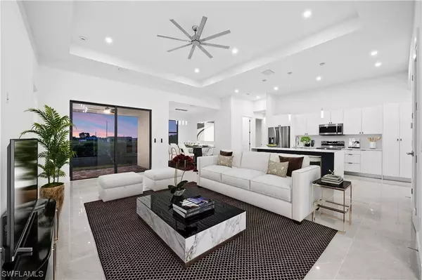 Virtually staged open-concept living room in Cape Coral new construction home featuring modern tile floors, tray ceiling, designer lighting, and dining area off the kitchen.