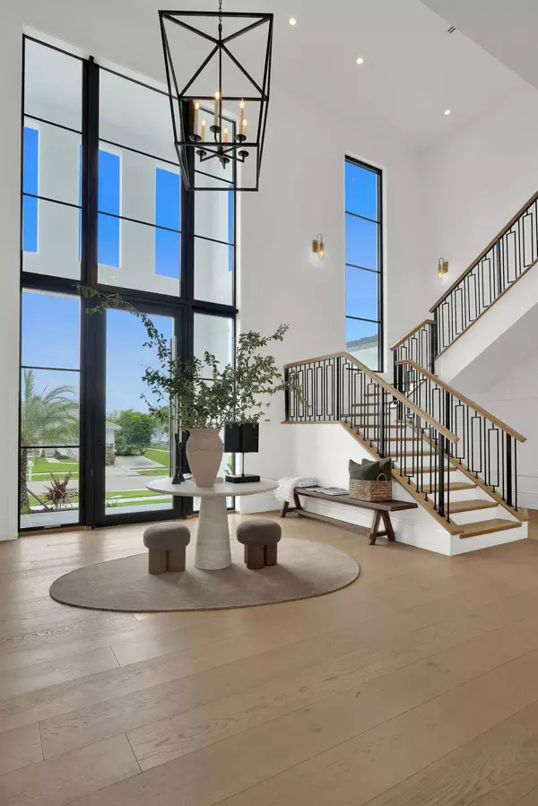 Grand 24-foot foyer at 839 Chestnut Court Marco Island with white oak flooring, custom iron staircase, and hurricane-impact glass pivot door