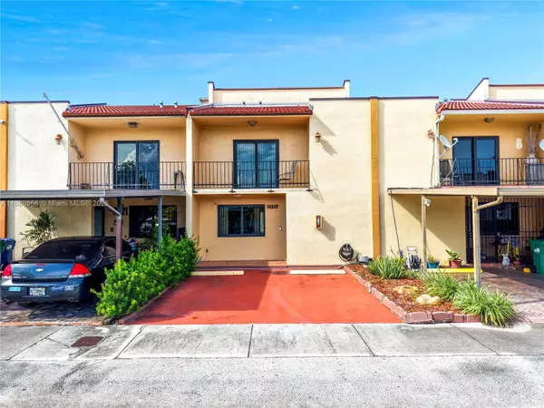 Front exterior of Sweetwater Miami townhouse at 11217 SW 1st St #5 featuring two stories, balcony, and two assigned parking spaces directly in front under a clear blue sky.