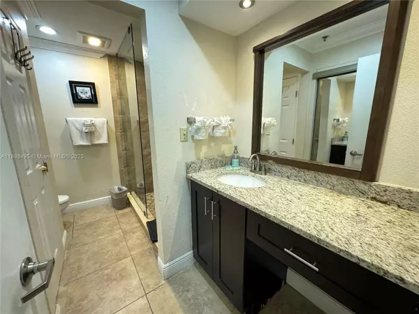 Modern bathroom in Kissimmee condo for sale near Disney World featuring granite vanity and glass shower.