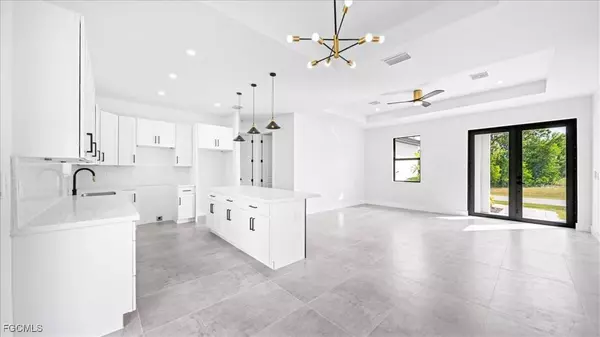 Open-concept kitchen and living room with white cabinetry, pendant lighting, and sliding glass doors at 3935 NW 45th Lane, Cape Coral.