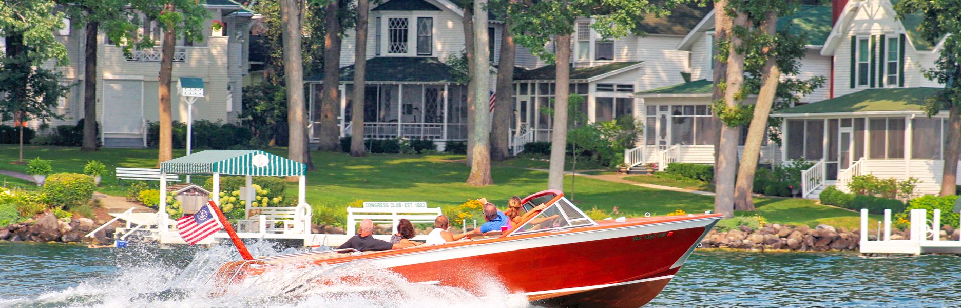 Classic Streblow runabout boat cruising past the historic Congress Club lakefront homes in Williams Bay on Geneva Lake