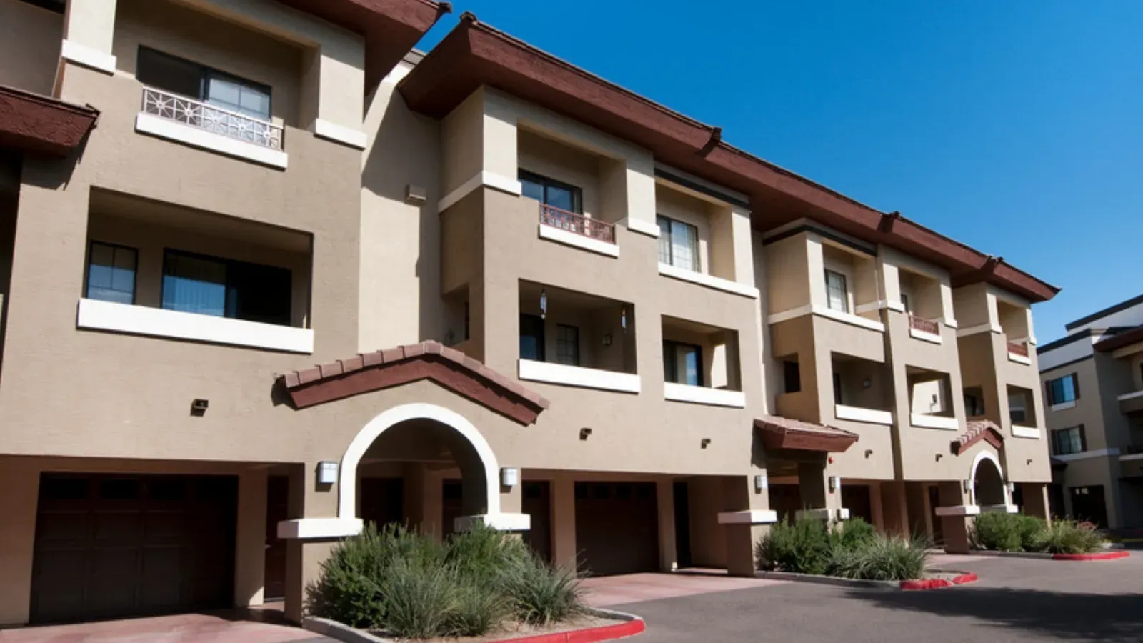 Row of tan stucco attached townhomes with garage doors along a desert street