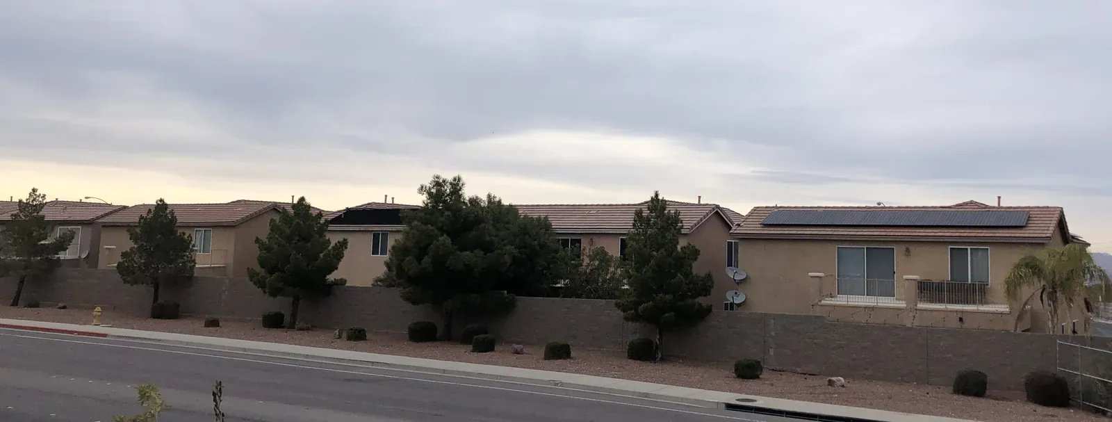 Row of residential stucco homes with tile roofs along a Henderson street under overcast skies
