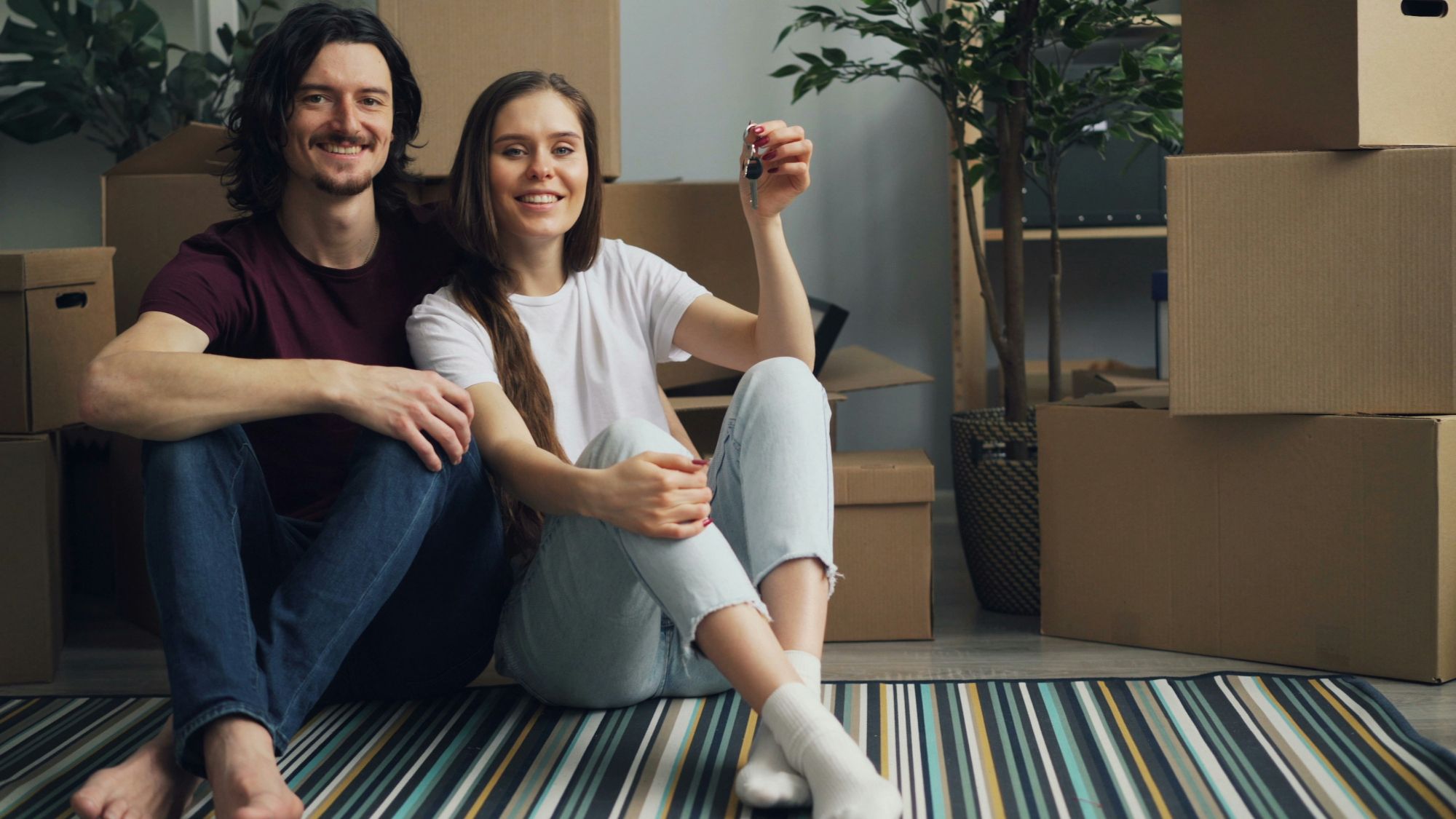 Happy young couple sitting on floor holding house keys, representing successful first time home buyers in Utah.