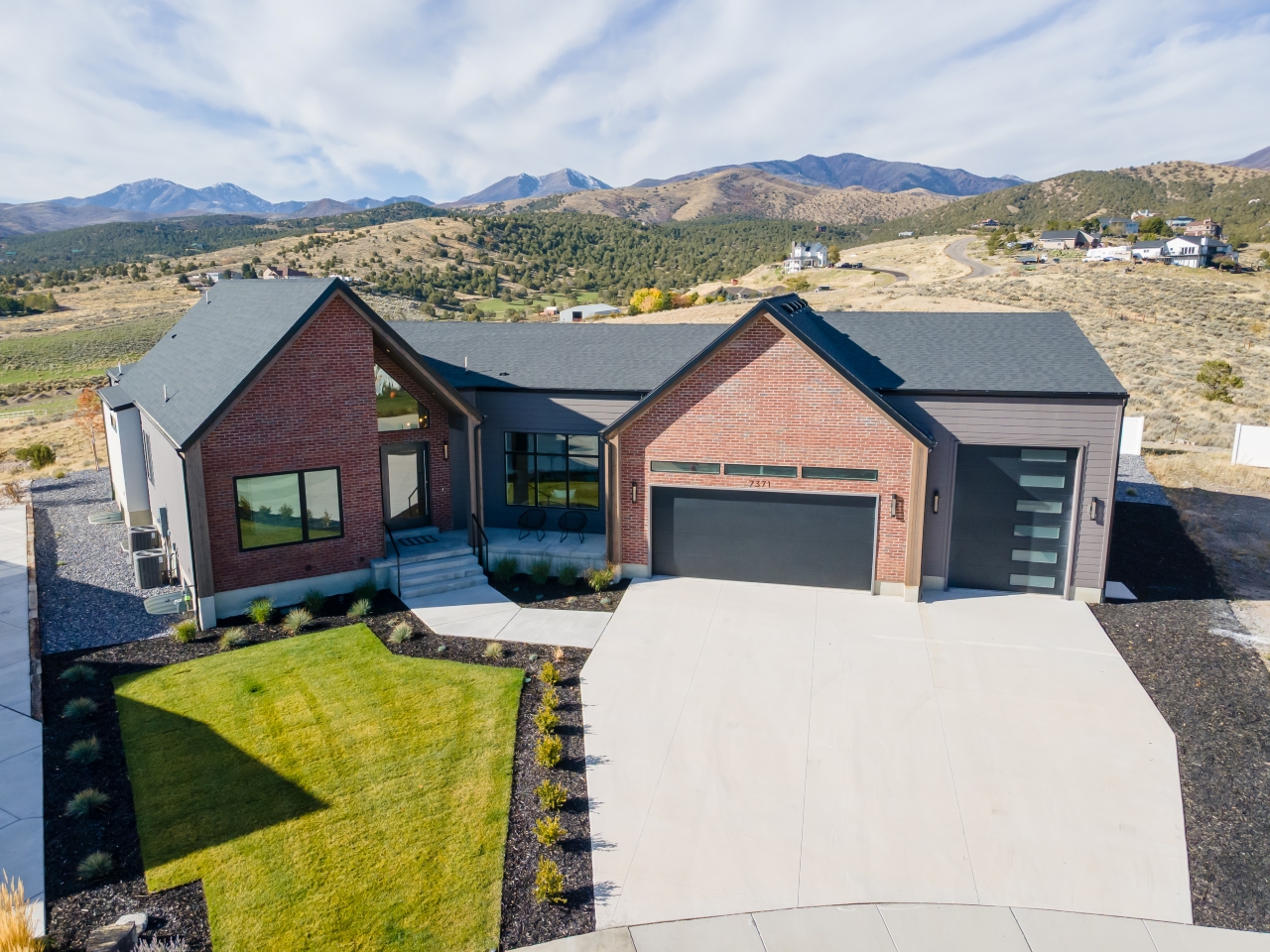 Front exterior of 7371 W Summit Crest Cir in Herriman, Utah - a modern luxury estate in Ridges at Rose Canyon featuring brick architecture, a 4-car garage, and panoramic mountain views.
