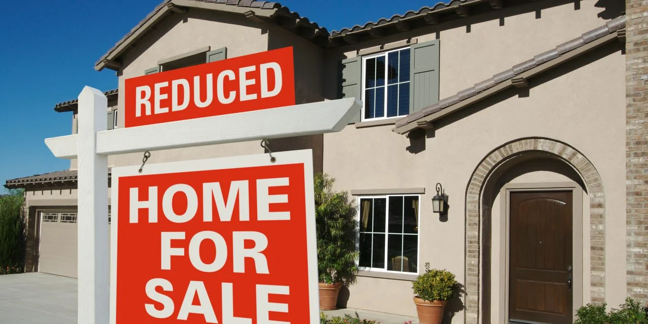 A home for sale with a prominent &ldquo;Reduced&rdquo; sign in front, representing a property that has been on the market longer than expected.