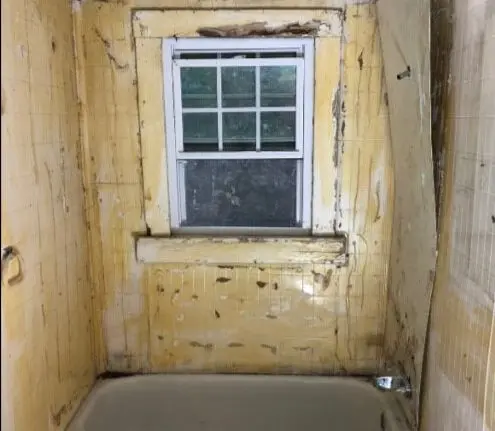 alt="Outdated bathroom with old bathtub, stained walls, and visible water damage before renovation"