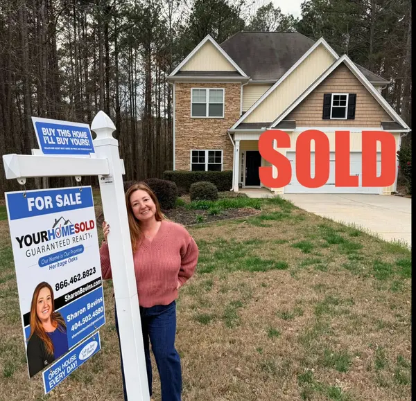 Sharon Bevins, Realtor in Villa Rica, standing with a SOLD sign and a "Buy This Home, I'll Buy Yours" rider in front of a West Georgia home.