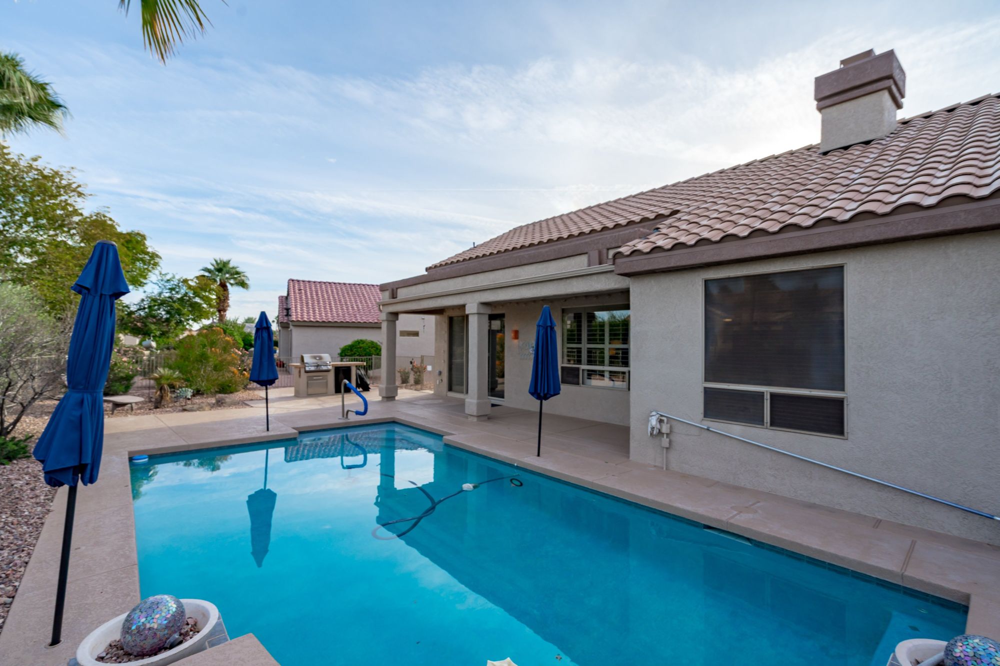 Private backyard of a Cholla model home in Sun City Grand, Surprise Arizona, featuring a heated saltwater swimming pool, covered patio, built-in BBQ area, low-maintenance desert landscaping, and resort-style outdoor living in a premier 55+ active-adult community.