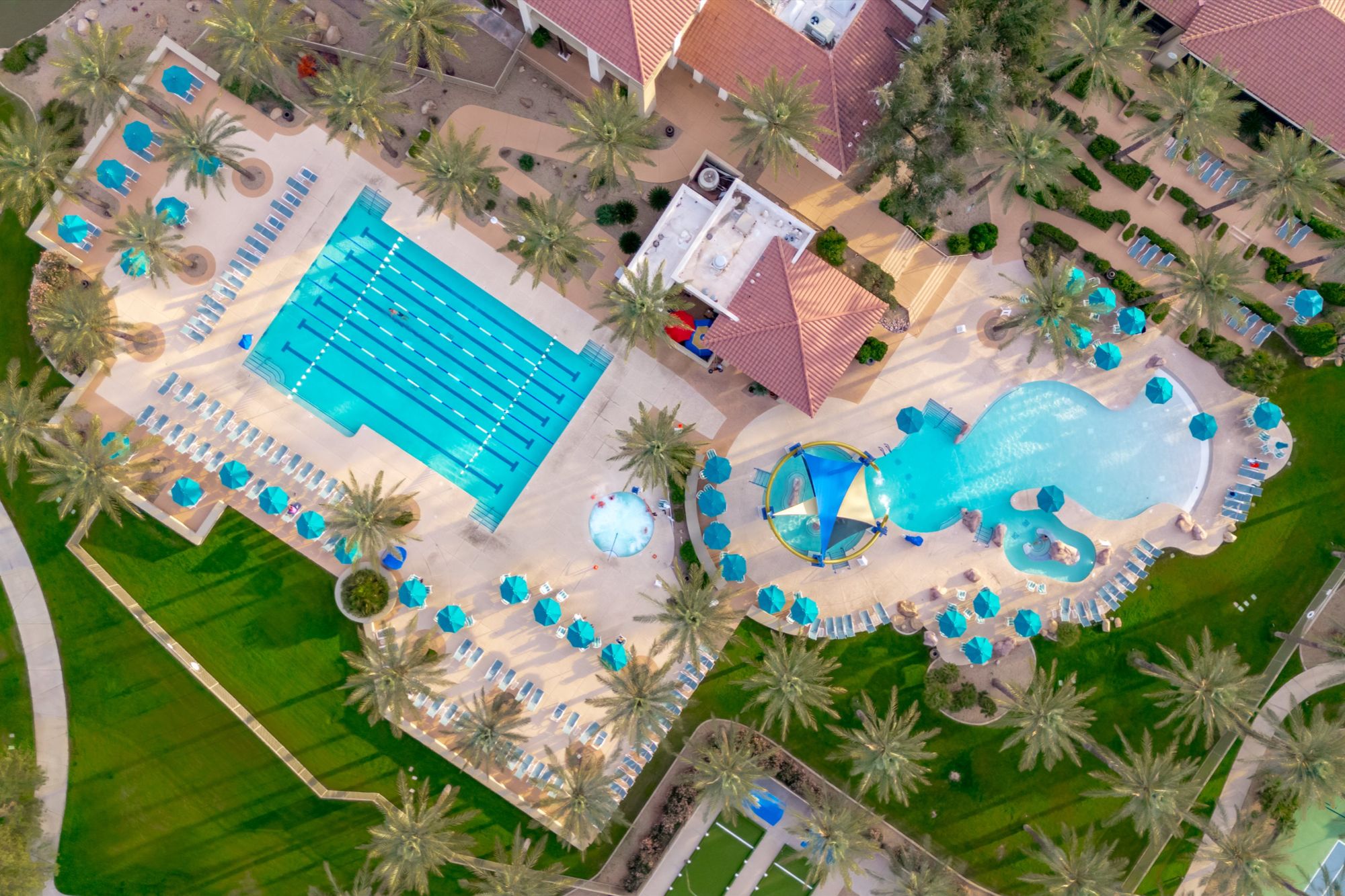 Aerial view of Sun City Grand recreation center in Surprise, Arizona, featuring resort-style swimming pools, lap pool, shaded lounge areas, palm-lined landscaping, and luxury amenities within a premier 55+ active-adult community.