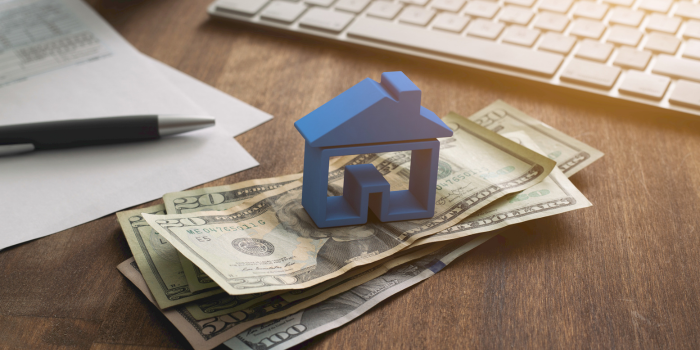 Blue house model on U.S. dollar bills with tax documents and keyboard — concept of real estate tax deductions and investment savings in 2025