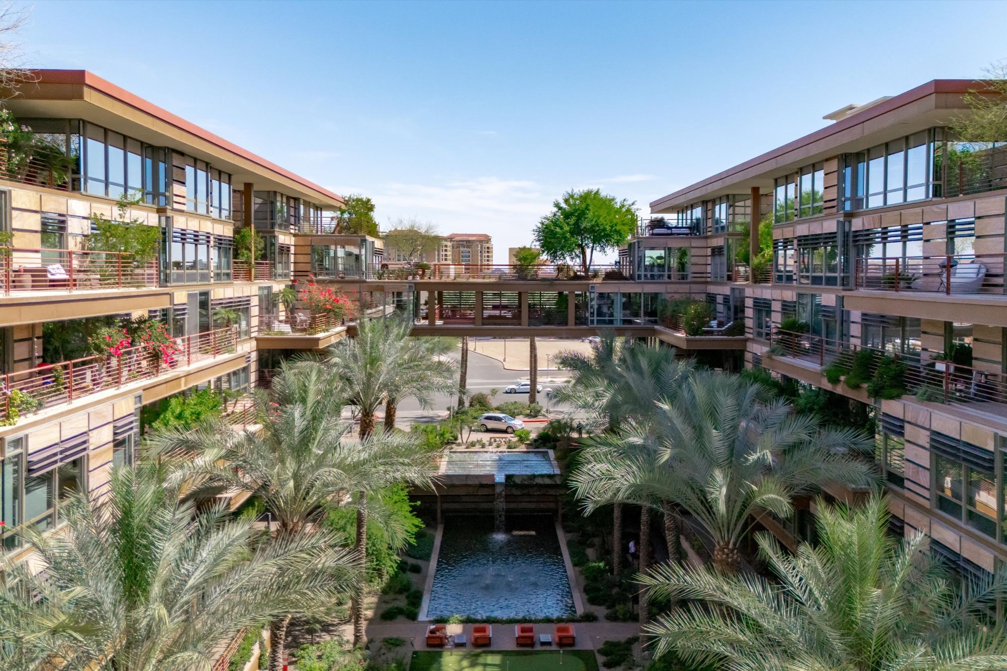 Interior courtyard view of Optima Camelview Village in Scottsdale, AZ, showcasing modern architecture, lush landscaping, water features, and luxury condos with private balconies. Located near Scottsdale Fashion Square and Old Town, this resort-style community offers mid-term and long-term rental opportunities, indoor/outdoor pools, fitness center, and on-site restaurant amenities.