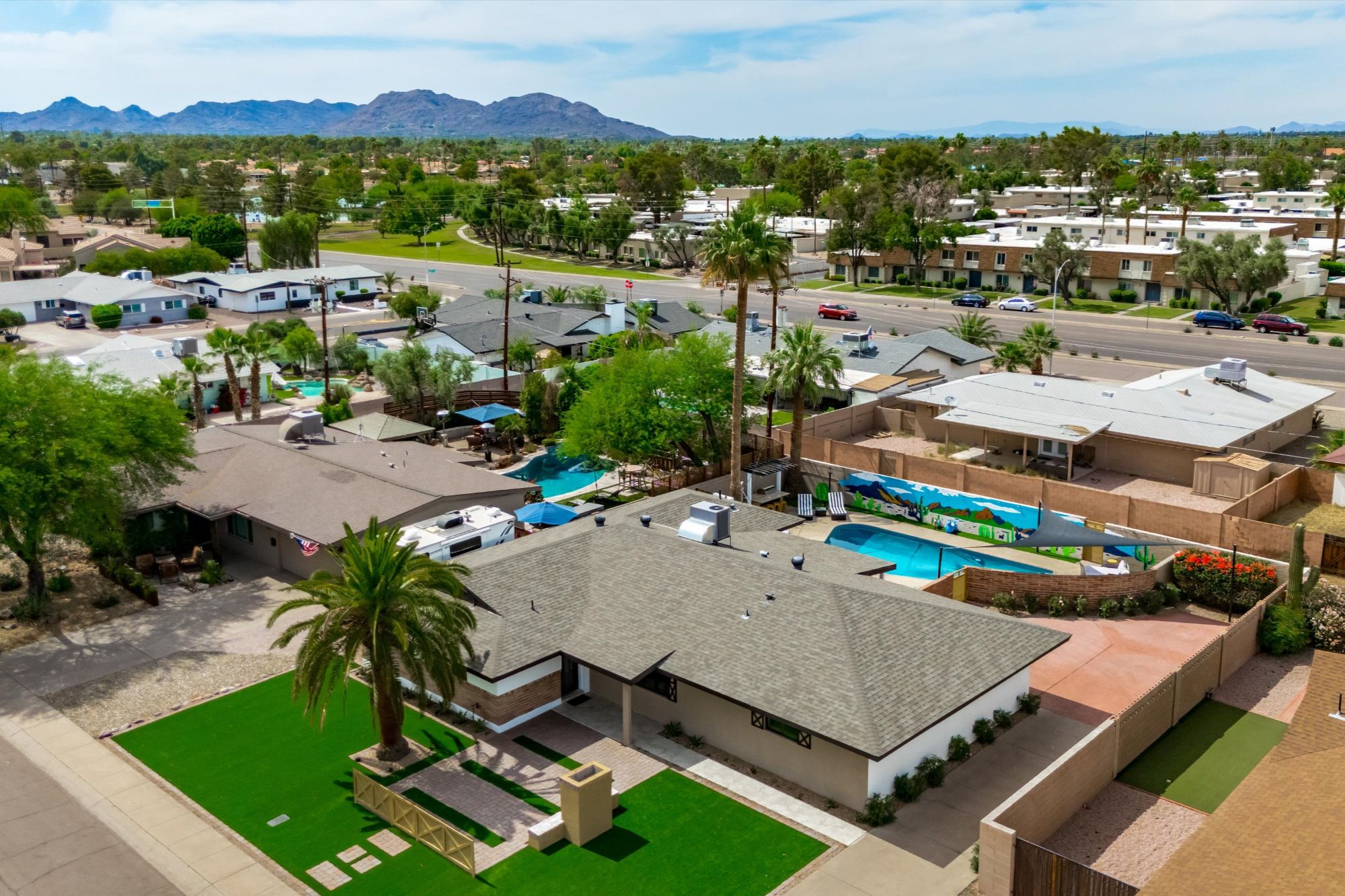 Aerial view of a fully renovated Scottsdale vacation rental featuring a resort-style backyard with a private pool, vibrant mural, lush front lawn with palm tree, and prime location near Camelback Mountain and Old Town Scottsdale—perfect for short-term rental income and upscale desert living.