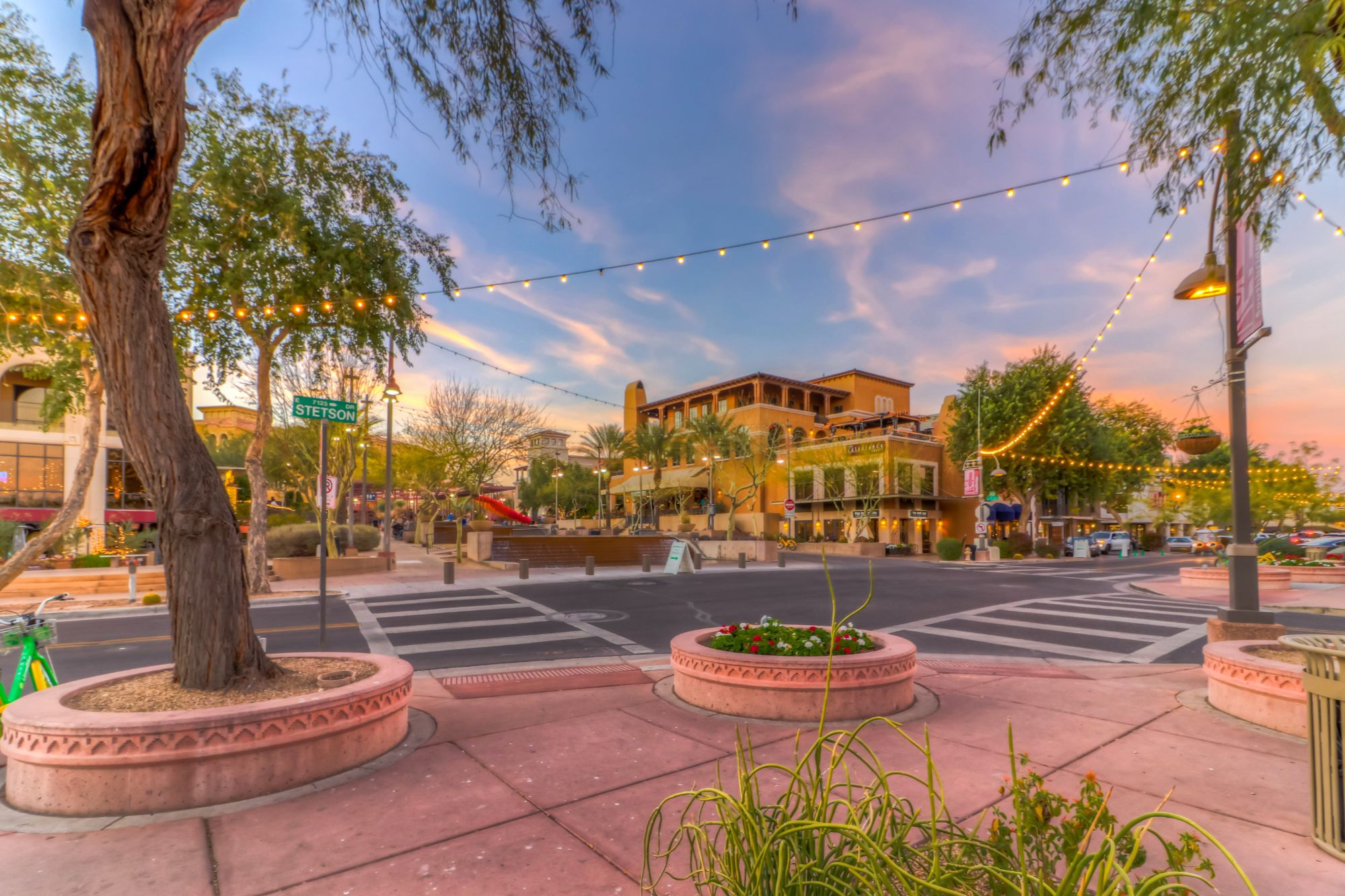 Vibrant evening view of Old Town Scottsdale at the corner of Stetson Drive, featuring string lights, palm trees, boutique shops, restaurants, and lively pedestrian walkways—highlighting the charm and nightlife near Scottsdale vacation rentals.