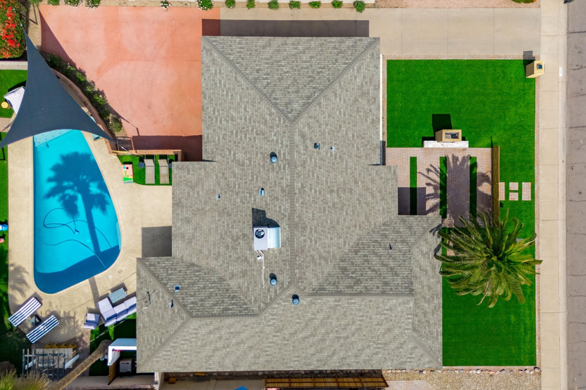 Top-down aerial view of a Scottsdale vacation rental showcasing a well-maintained roof, private backyard with pool and shaded lounge area, spacious patio, and lush green front yard with palm tree and modern landscaping—ideal for short-term rental guests seeking privacy and resort-style amenities.