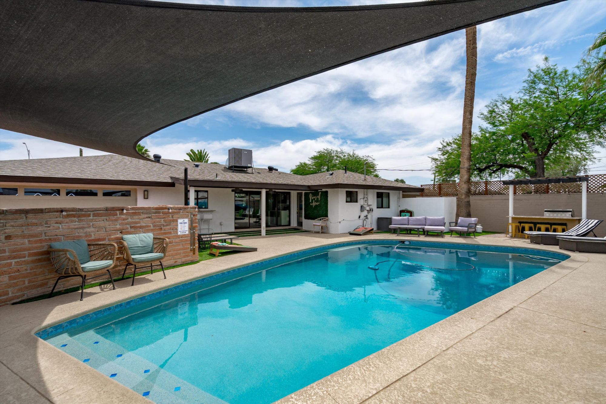 Backyard oasis at a Scottsdale vacation rental featuring a private swimming pool, shaded lounge area, outdoor bar with seating, BBQ grill, and cozy patio furniture—perfect for entertaining, relaxing, and enjoying Arizona’s sunny weather.