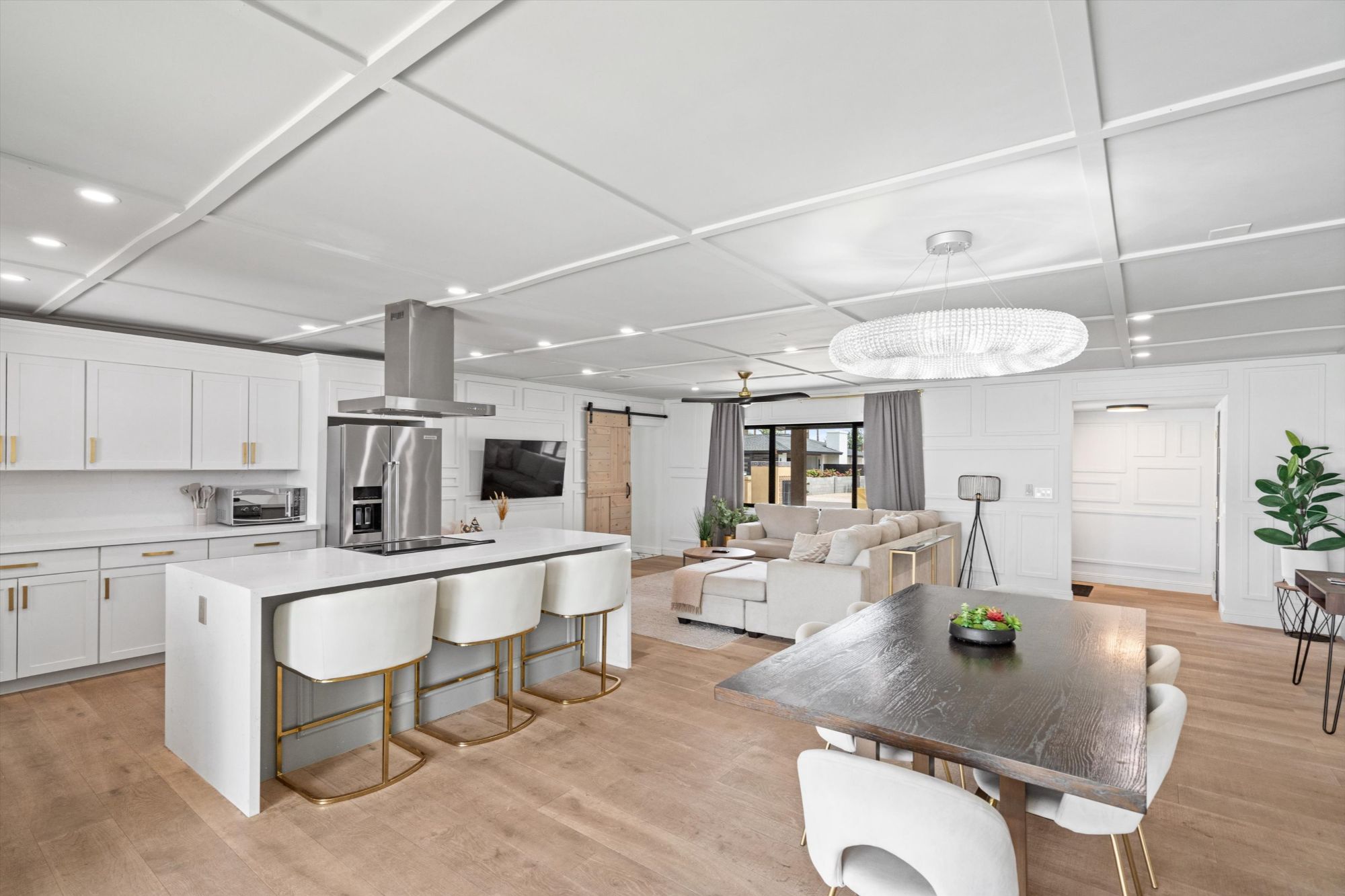 Luxury open-concept interior of a Scottsdale vacation rental featuring a modern kitchen with white shaker cabinets, quartz countertops, stainless steel appliances, and gold-accented barstools—seamlessly flowing into a stylish dining area and cozy living room with elegant finishes and natural light.
