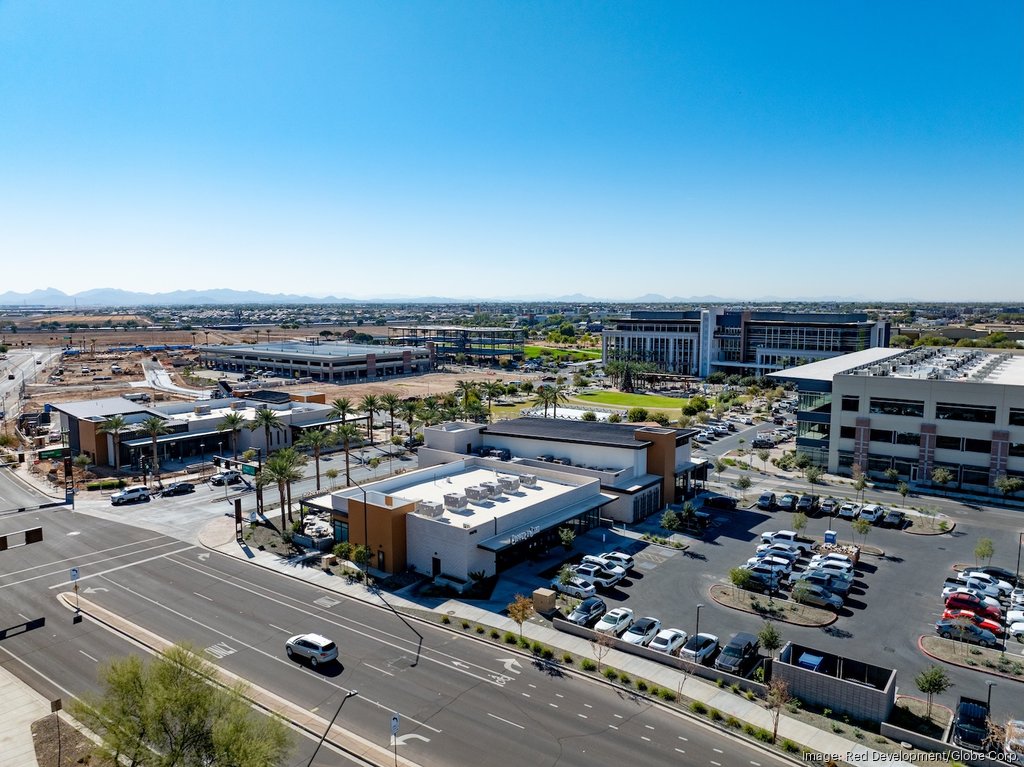 Aerial view of GSQ development site in Goodyear, Arizona, highlighting future home of Trader Joe’s surrounded by commercial buildings, new construction, and palm-lined streets with the Estrella Mountains in the background.