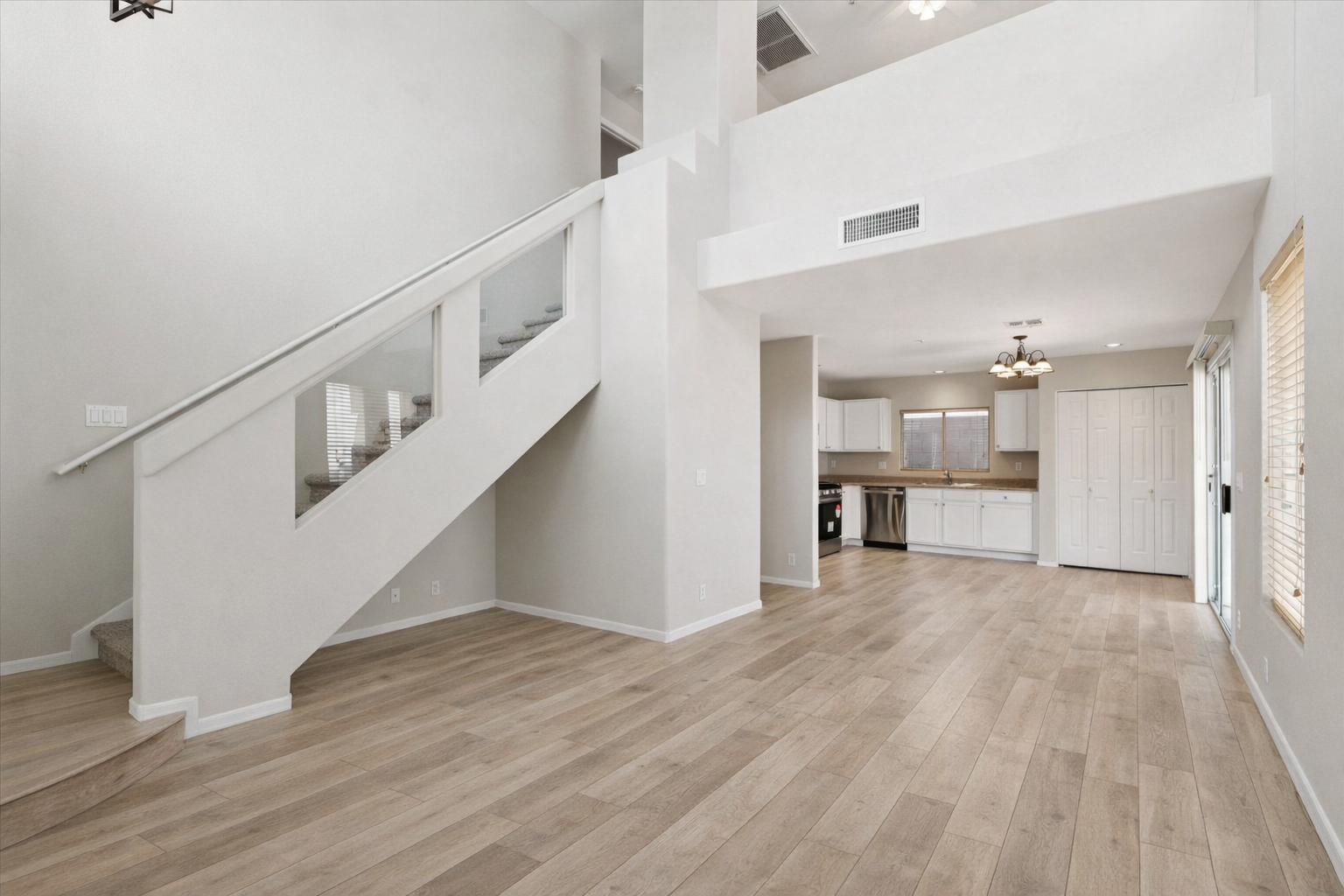 Open-concept living space in North Scottsdale single-family home featuring updated wood-style flooring, vaulted ceilings, staircase, and adjacent kitchen in gated Scottsdale community