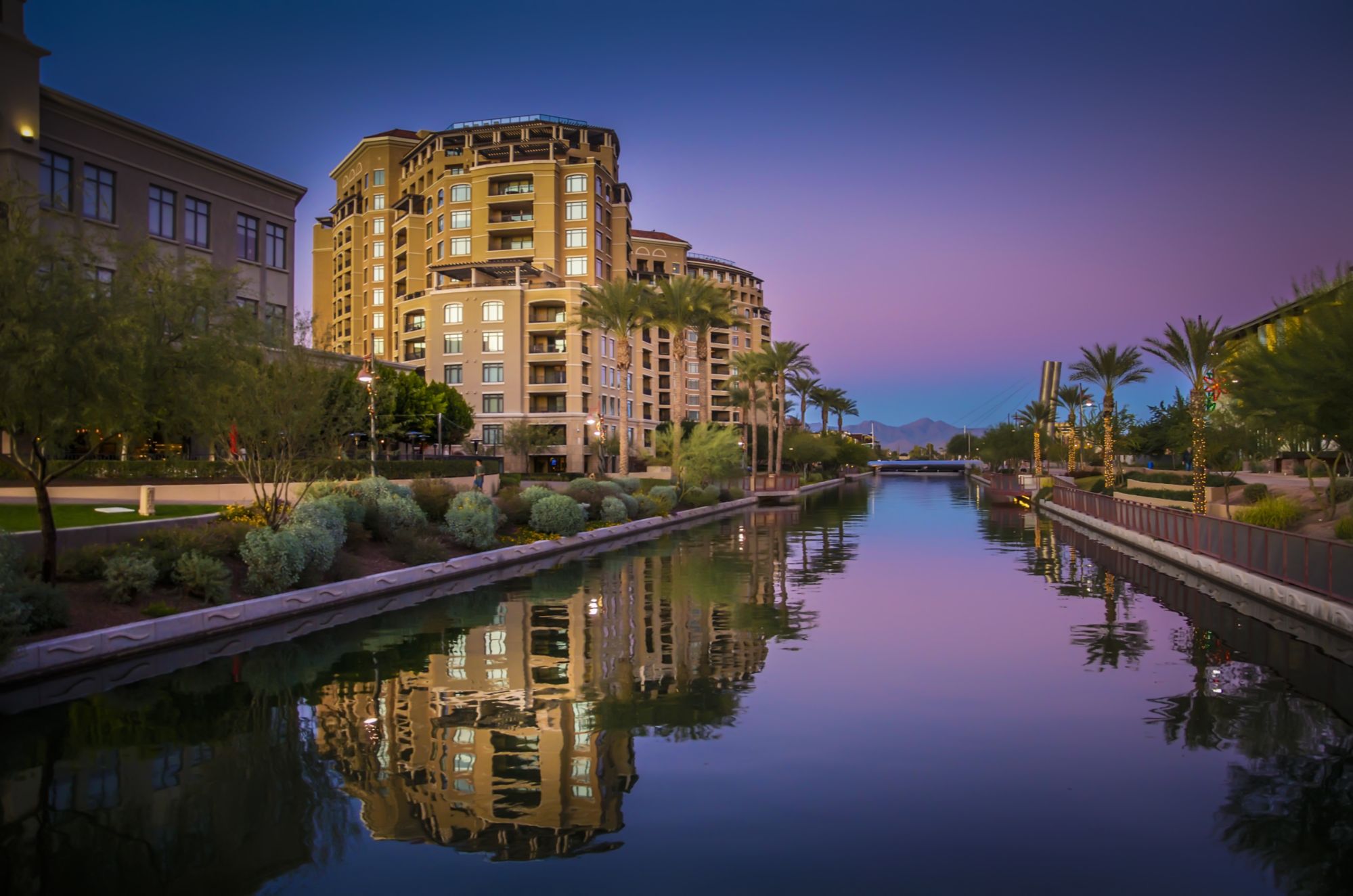 Scottsdale Arizona waterfront canal at sunset with luxury condos, palm trees, and mountain views near Old Town Scottsdale, showcasing lifestyle, walkability, and strong demand for vacation rentals and real estate