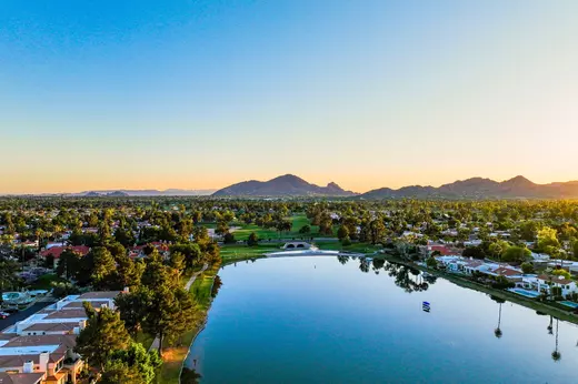Springtime in Arizona with clear skies, bright sunshine, and calm lake views surrounded by lush green neighborhoods and mountain backdrops, showcasing the mild weather and outdoor beauty that attract people to move to Arizona.