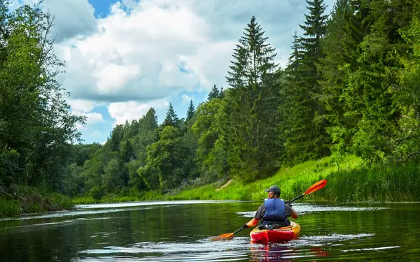 Kayaker paddling a calm river lined with green forest