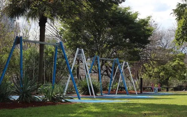 Sunny playground with swings surrounded by lush green trees and shade