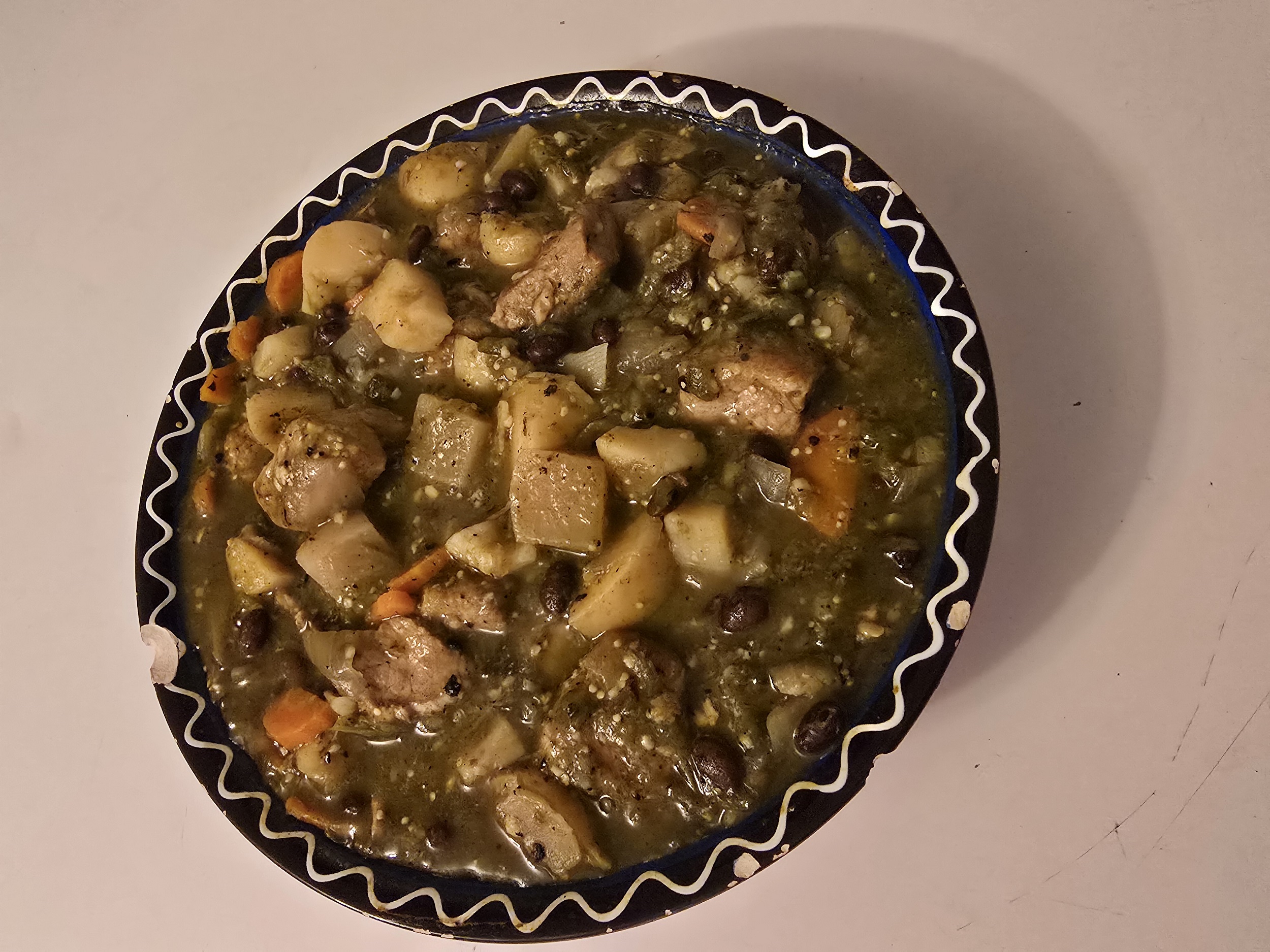 A serving bowl filled with hearty Pork & Green Chile Stew. The dish features chunks of pork, potatoes, carrots, black beans, and tomatillo-green chile broth, creating a rich and colorful Southwestern comfort food.