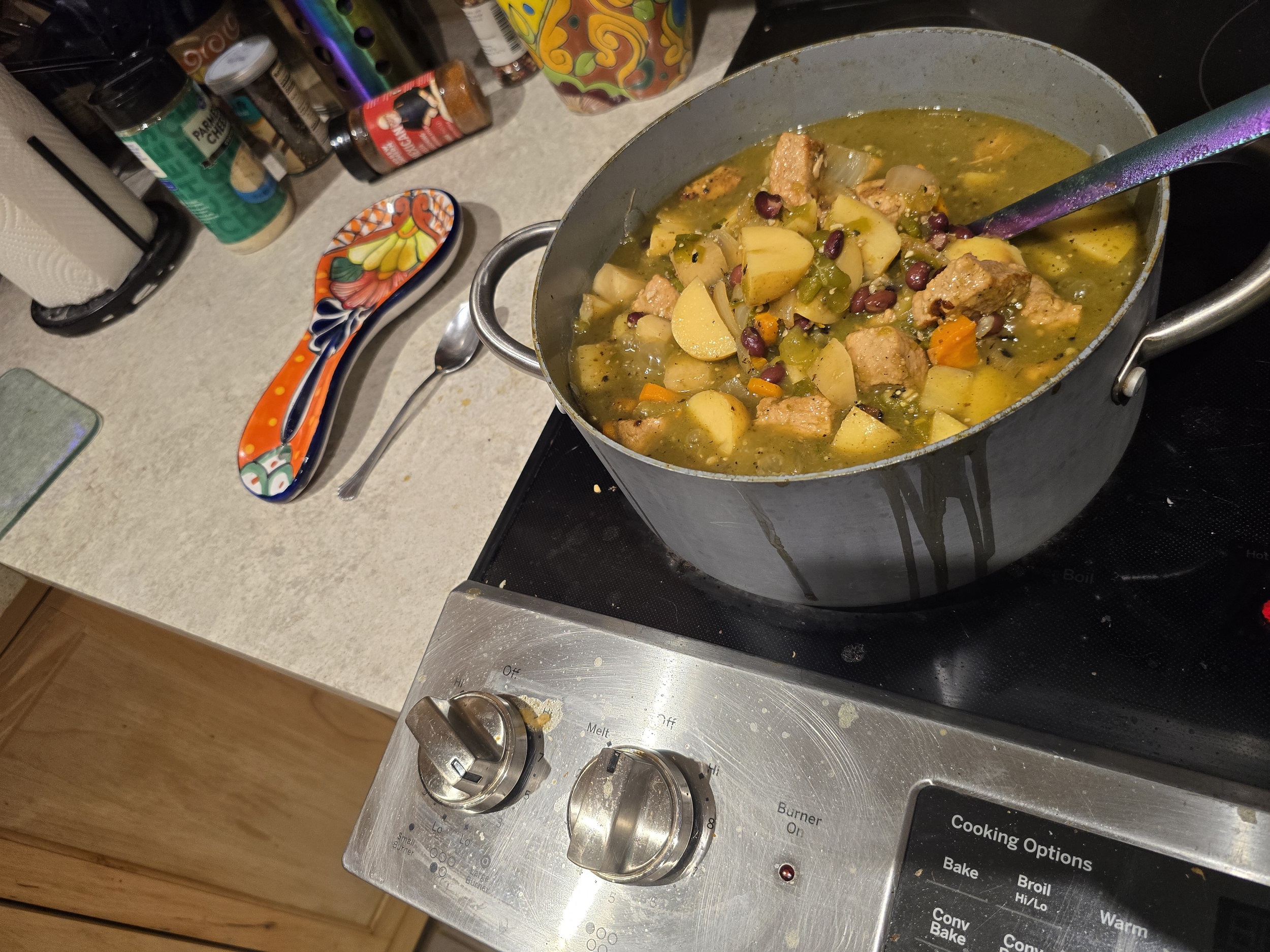 A pot of Pork & Green Chile Stew simmering on the stove. The mixture of diced vegetables, pork, and black beans is cooking in a flavorful green chile broth, with a bright, rustic kitchen setting around it.