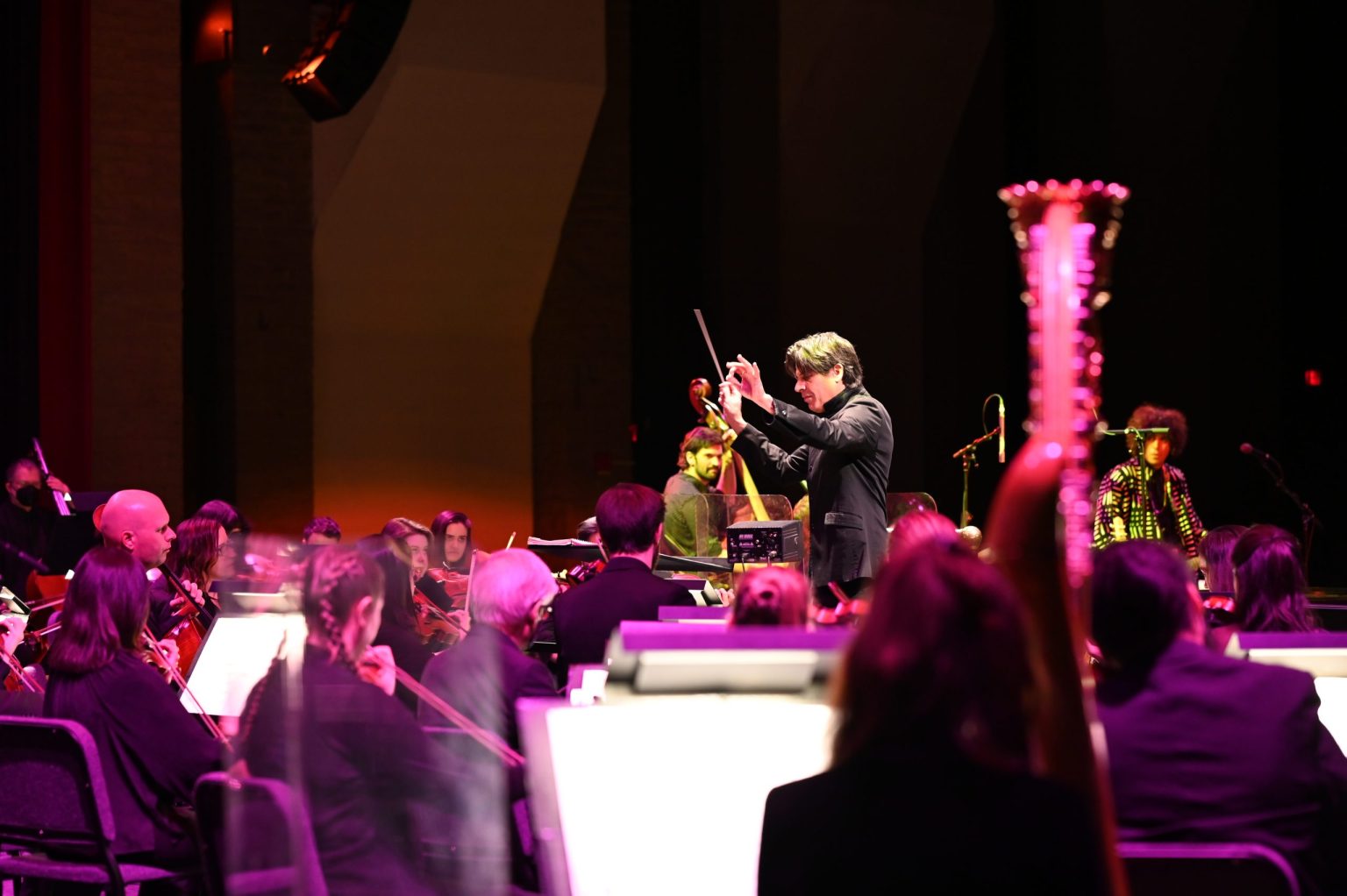 Conductor leading the Tucson Symphony Orchestra onstage with musicians playing under warm, colorful lighting