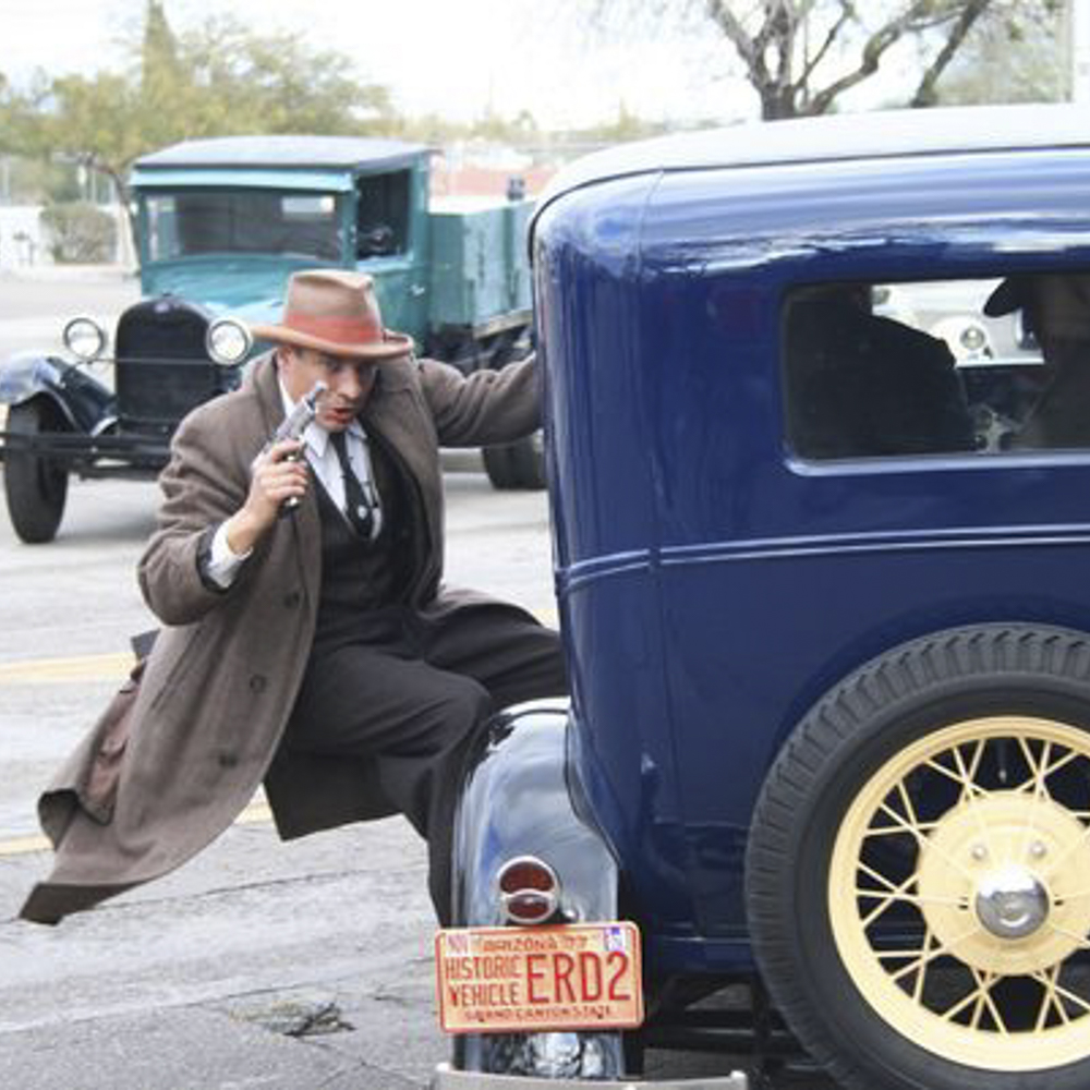 Historical reenactor dressed as John Dillinger stepping out of a vintage car during a Dillinger Days reenactment in downtown Tucson.