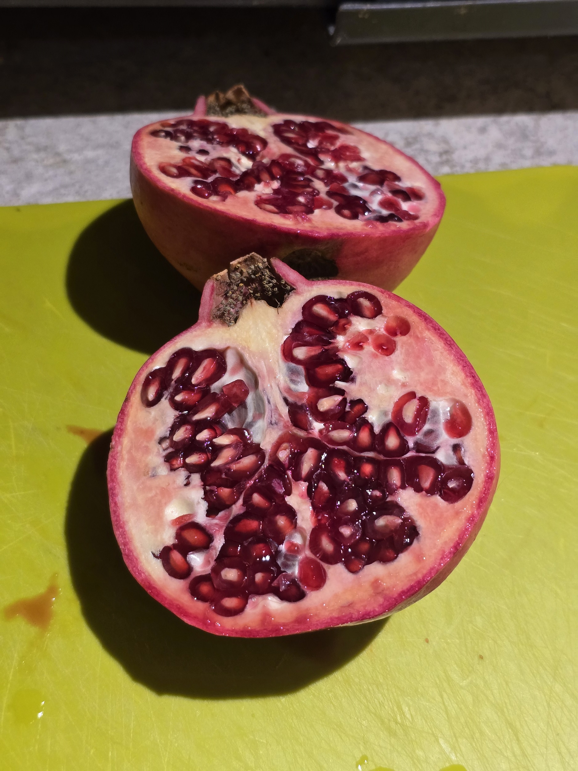 A fresh pomegranate cut in half on a cutting board, seeds exposed