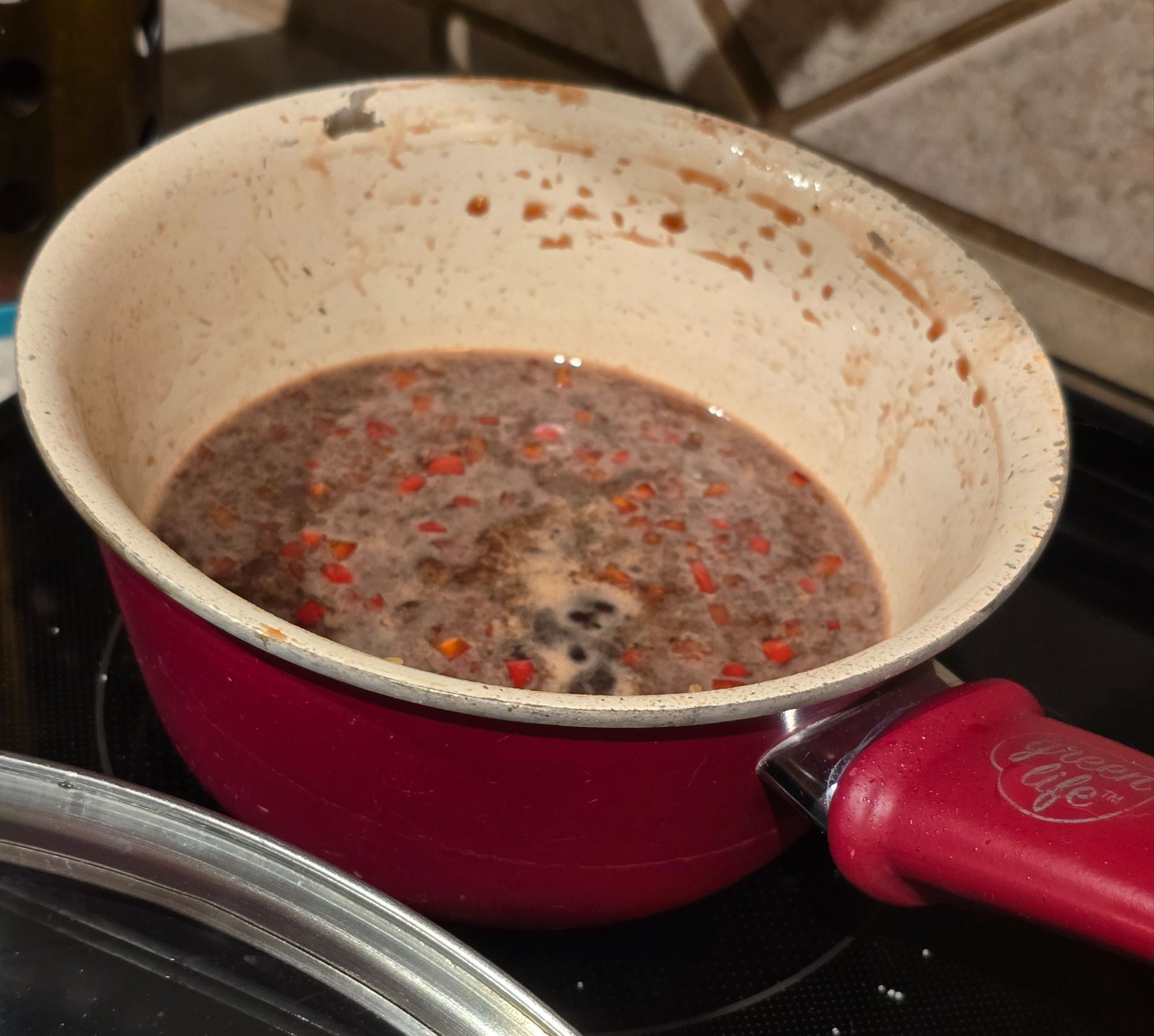 Pomegranate glaze reducing in a saucepan, flecked with red chile