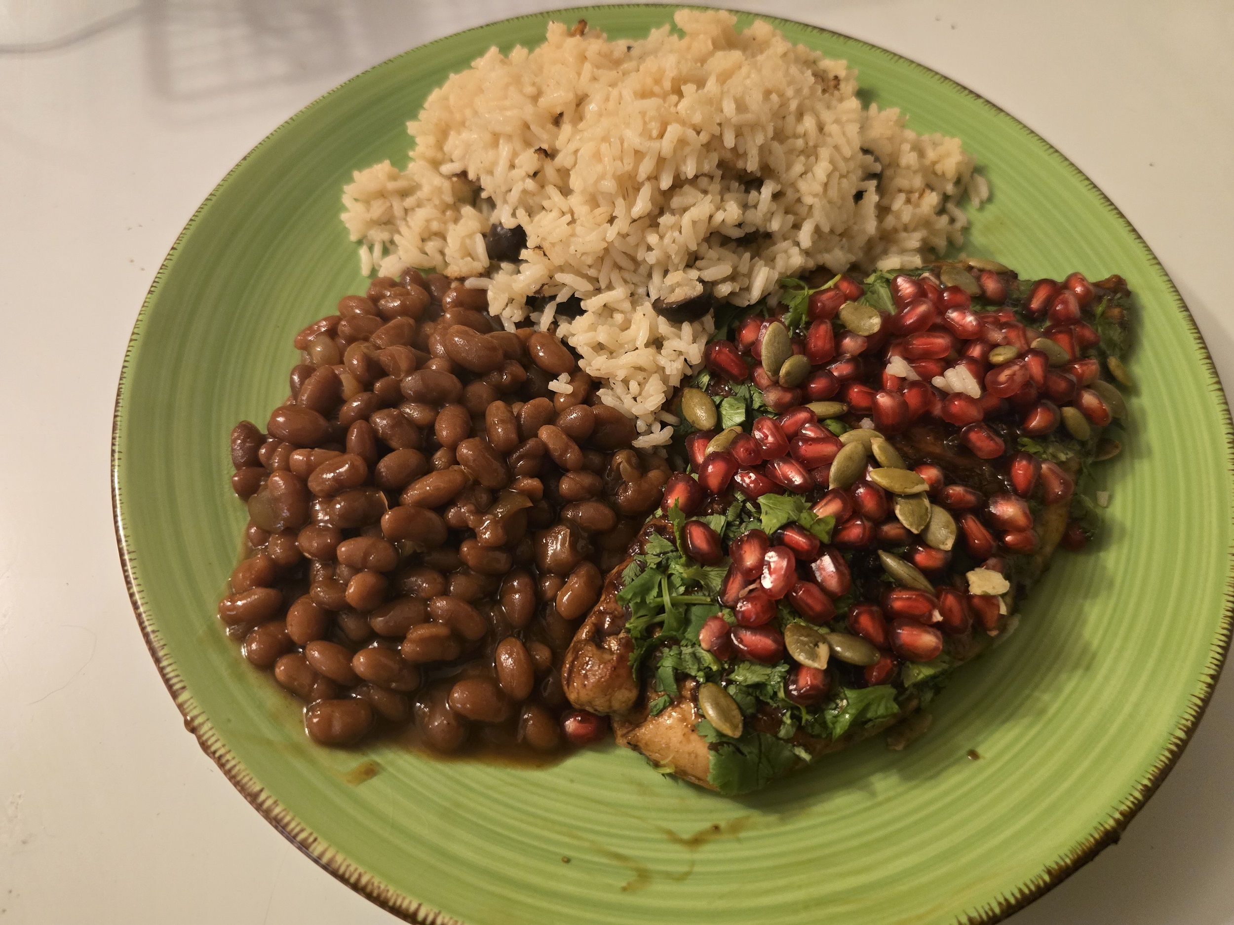 A plated serving of pomegranate-glazed chicken with rice and pinto beans