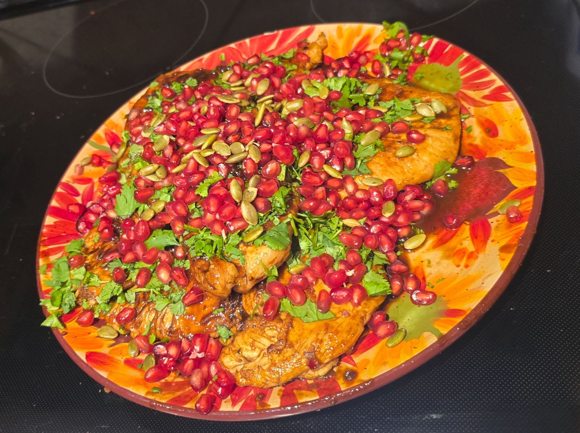 Pomegranate-glazed chicken breasts on a painted Talavera platter, covered in pomegranate seeds, toasted pepitas, and chopped cilantro
