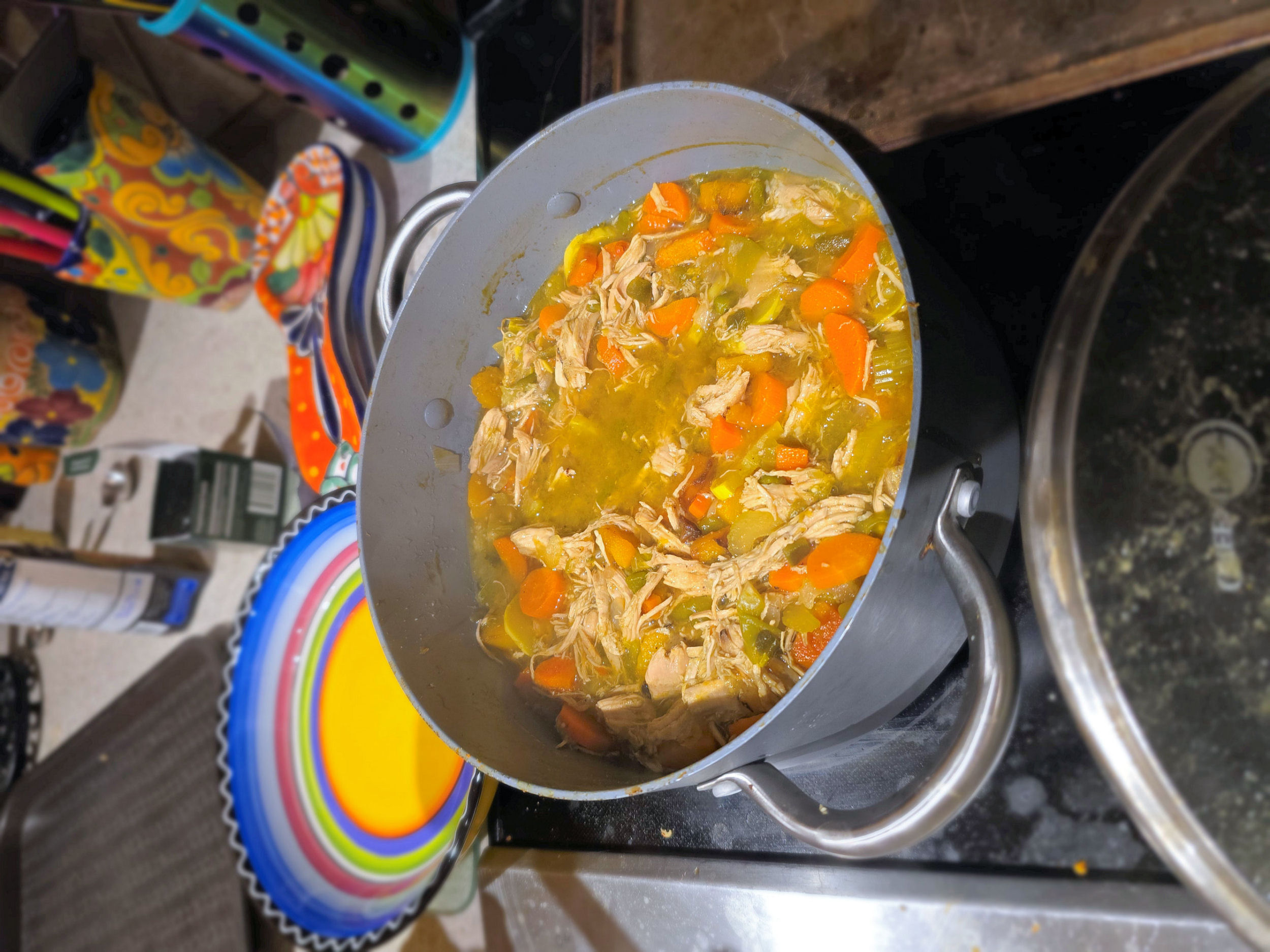 Large pot of homemade spicy chiltepin chicken soup simmering on the stovetop, filled with shredded chicken, carrots, celery, tomatillos, and butternut squash in a golden broth.