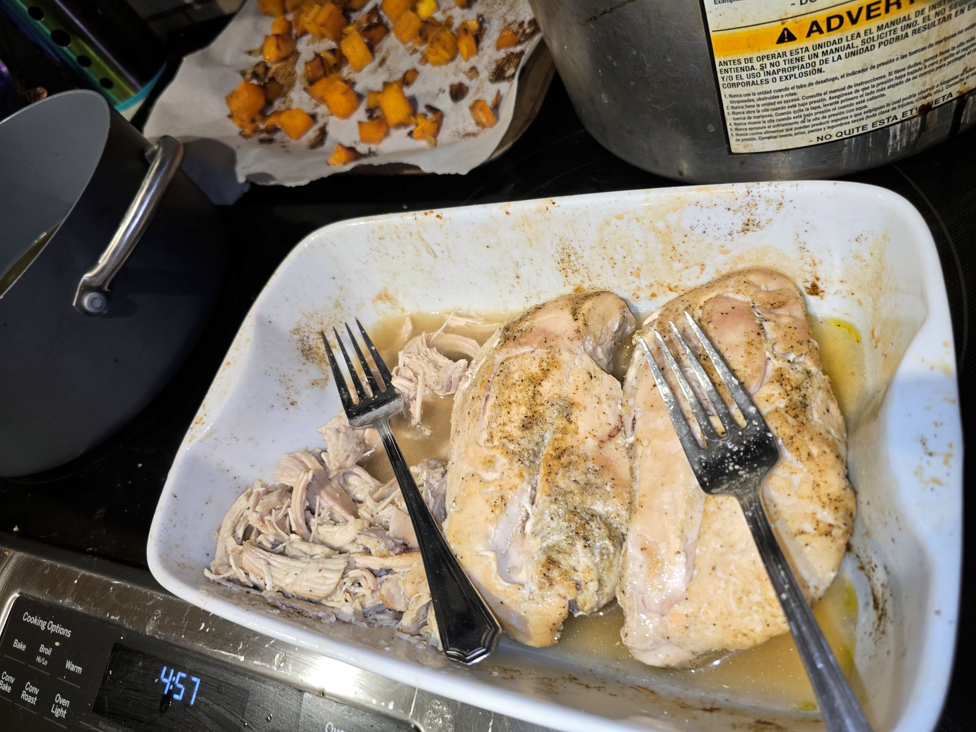 Cooked chicken breasts resting in a baking dish with pan juices, partially shredded and ready to be added to soup.