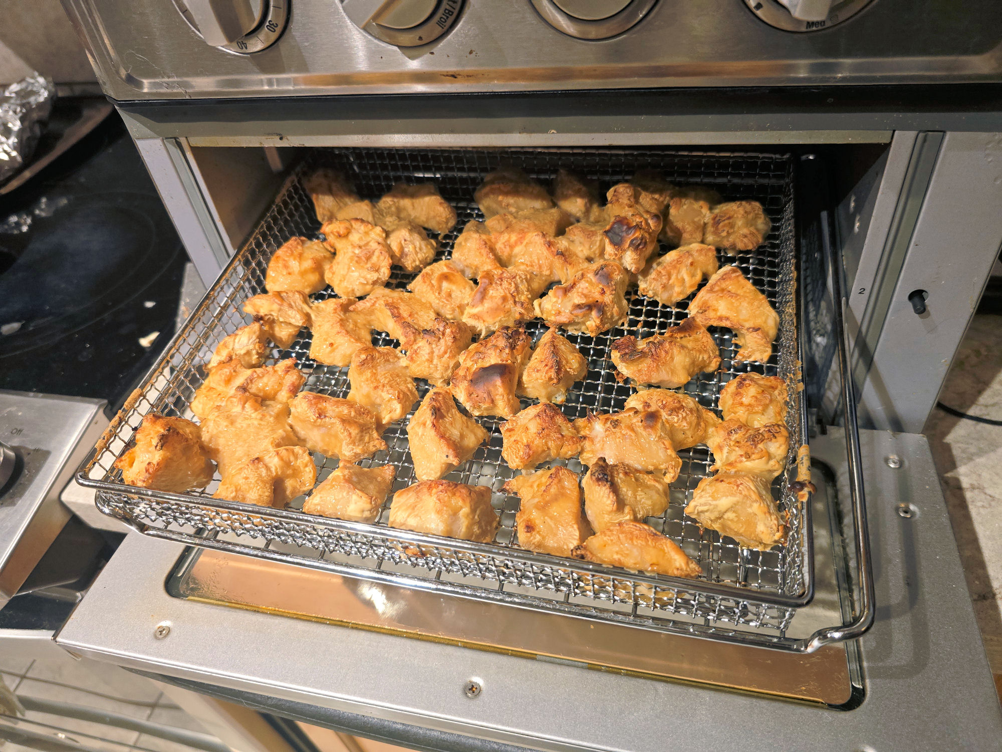 Air fryer basket filled with bite-size pieces of chicken cooking until golden and crispy, prepared for Chinese-style lemon chicken.